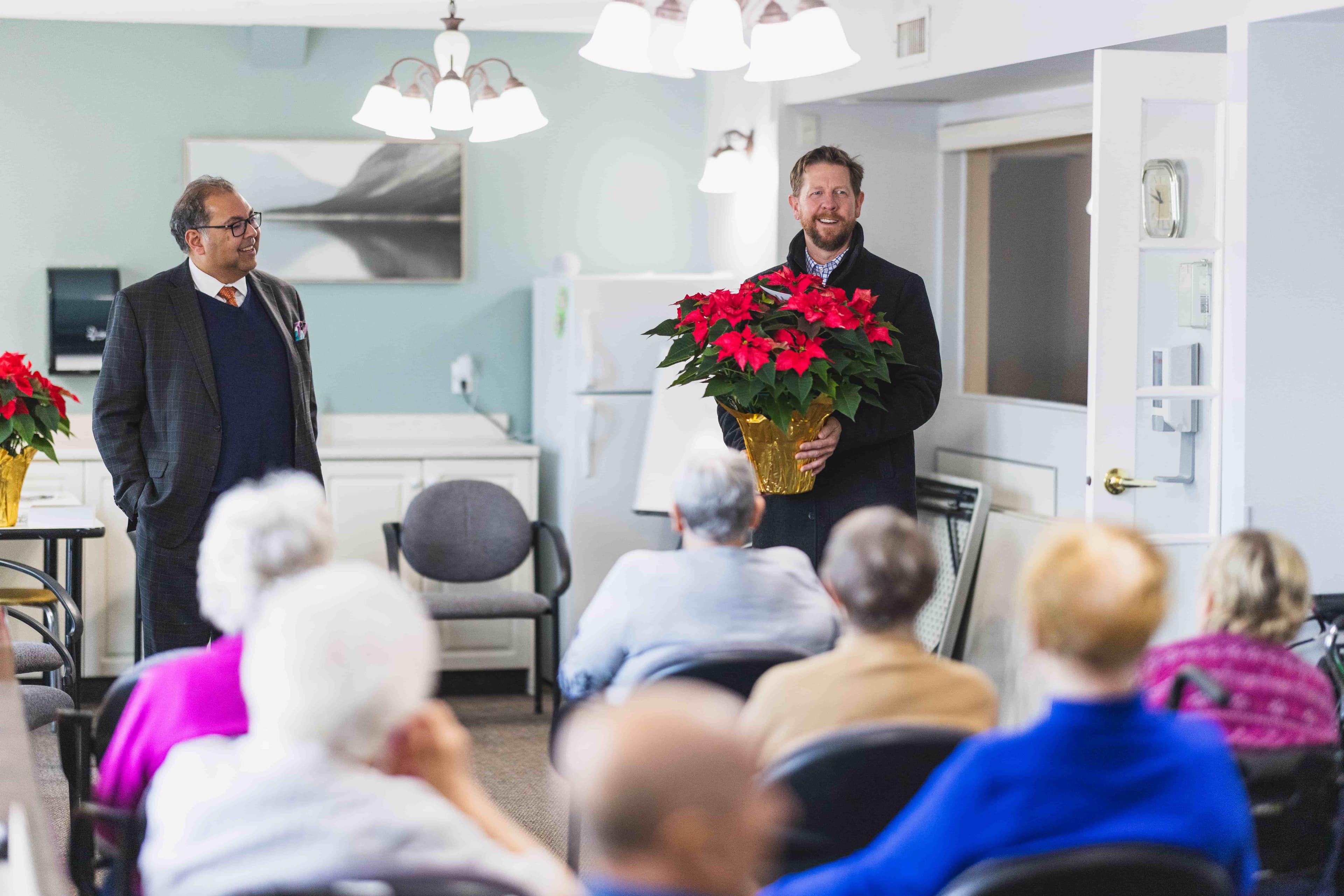 Kyle Kasawski and Naheed Nenshi gift a poinsettia to a senior's residence in Sherwood Park.