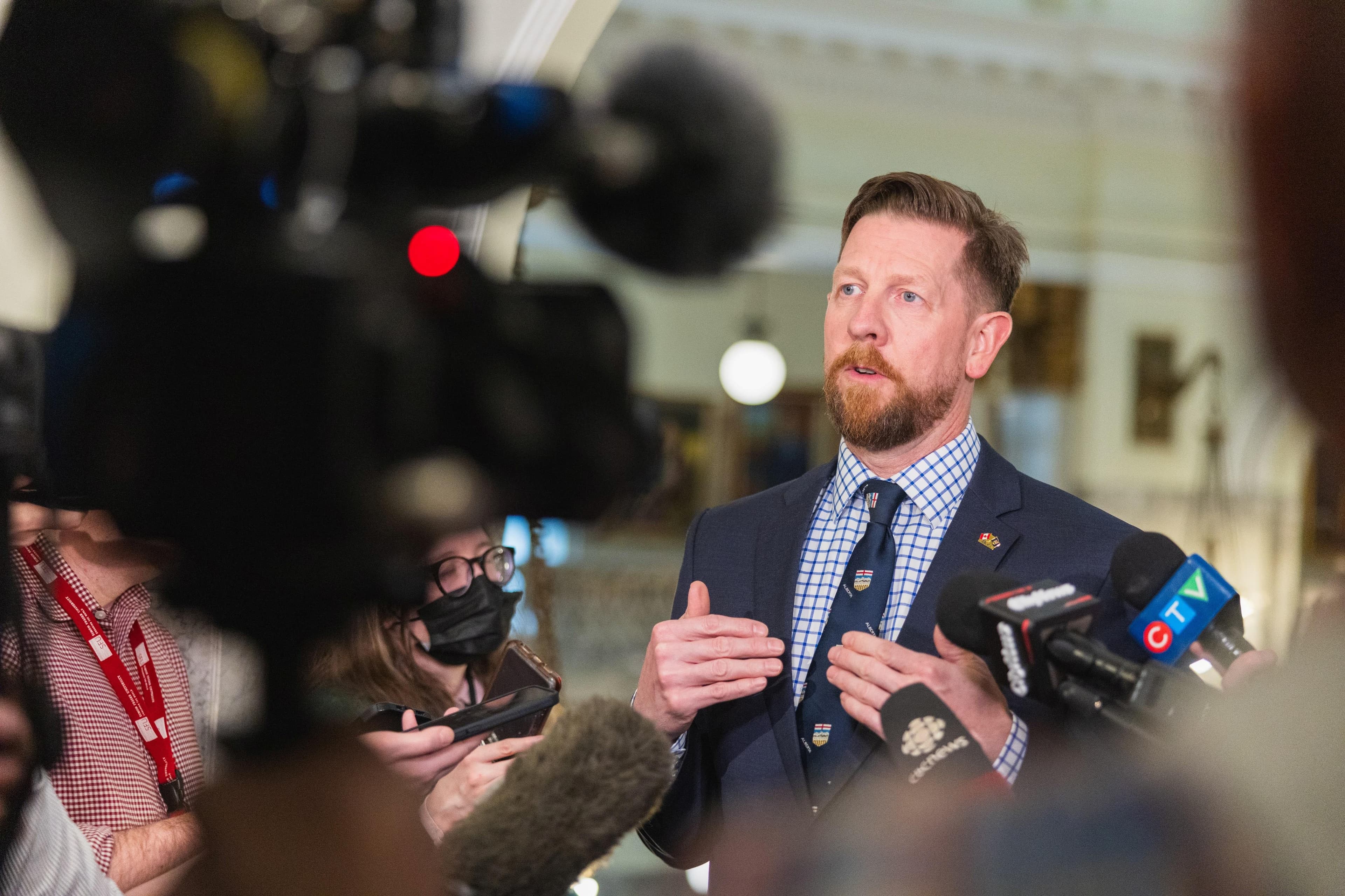 MLA Kyle Kasawski stands before a group of microphones and cameras at a media scrum.