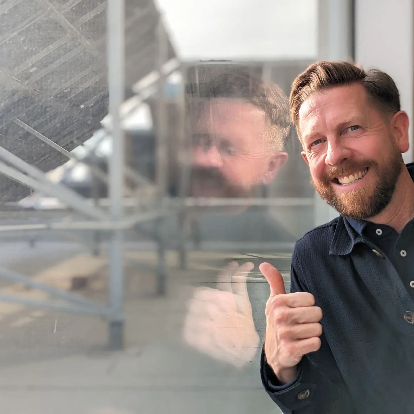 MLA Kyle Kasawski give a thumbs up while standing beside a rooftop solar array at the Northern Alberta Institute of Technology.